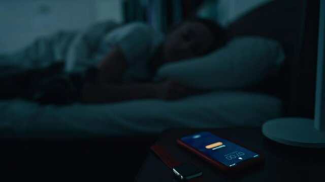Young sleeping woman wakes up early in morning to disable activated smartphone alarm on bedside table. Wake up for running. Cinematic shot. High quality 4k footage