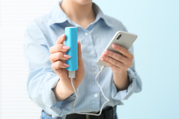 Young woman with smartphone and power bank near blue wall, closeup