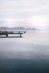 General plan of the pier for fishermen, which is located on a misty lake. The mist on the water creates the feeling of a magical effect. Clouds bounce off the surface. Place for text