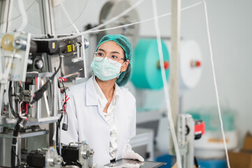 Both male and female Asian scientists are outfitted with protective gear. Examining the factory's machinery and materials used in the mask-making process. Covid 19 is a piece of preventive equipment.