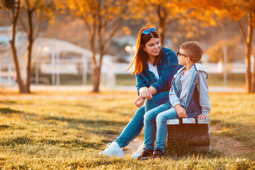 Autumn season. A young mother and her son are sitting together on a park bench. The concept of a happy childhood