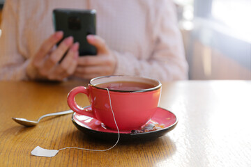 Cup of hot tea on table in cafe and woman on background