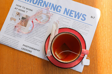 Cup of hot tea, newspaper and eyeglasses on wooden background