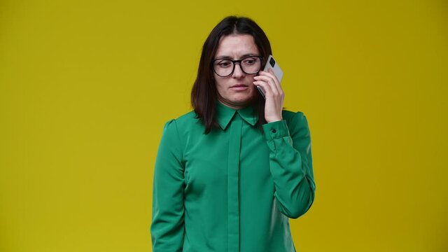 the woman received a call and was told unpleasant news, she became very passive and angry, she says no, she is brunette, short-haired, wears glasses, is wearing a green shirt, the background is yellow