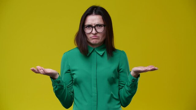 a woman looks at the camera and shows no head, not good, she does not like it, she wears glasses, dark-haired, short hair, dressed in a green shirt, the background is yellow