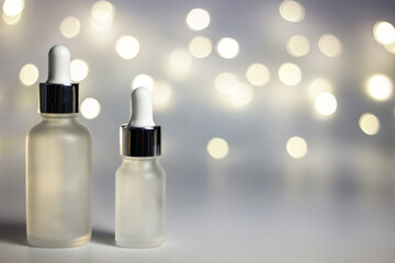 White background with warm yellow round bokeh. Copyspace. New Year's holiday lights. Christmas. Glass cosmetic jars with a pipette. Artificial Christmas tree