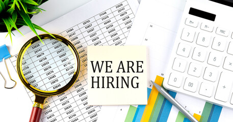 WE ARE HIRING text on sticker on diagram with magnifier and calculator. Business concept