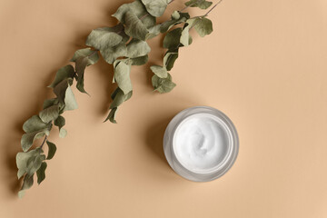 White cream jar on beige background close-up. Beauty cosmetics presentation with dry flower. Moisturizing skincare product. Top view. Trendy healthcare concept. Copy space for design. Flat lay style