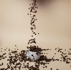 Spilling coffee beans on white coffee cup. Light brown background.