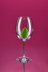 Christmas tree made of ginger cookies with icing stands in an empty glass on a high thin leg on a burgundy background with a reflection. Christmas menu. Vertical image. Copy space.