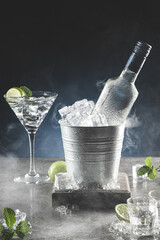 Bottle of ice cold vodka in bucket of ice and glasses on dark background with copyspace. Vertical...