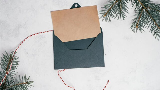 Stop motion video of green opening envelope on white background with branches of Christmas tree. Kraft paper card is taken out of new year envelope and opened. Copy space. Top view
