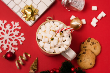 Christmas Home Office Desk with White Keyboard Christmas Golden Ornaments Cup of Cocoa with Marshmallw and Candy Cane Cookies and Red Candle Red Background Top View