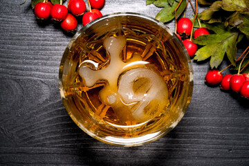 glass of whiskey with ice in the shape of a skull next to a viburnum branch on a black background