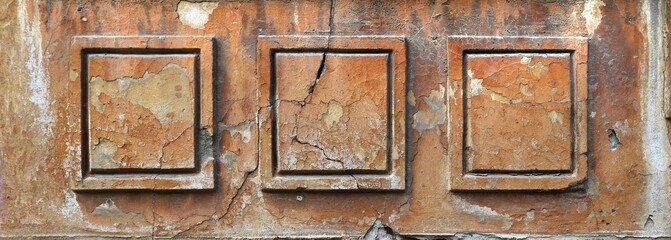 Rough facade of an ancient house with framed square ornaments with cracks, chipped orange painting and moisture - weathered texture for an horizontal background banner