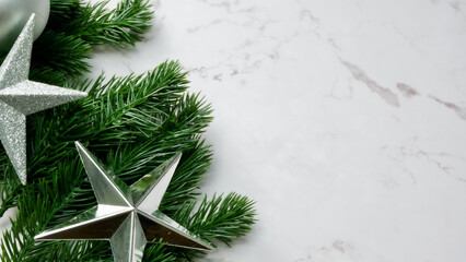 Green pine tree leaves on white marble background, christmas decorations in bright silver color. Simple and creative christmas concept.