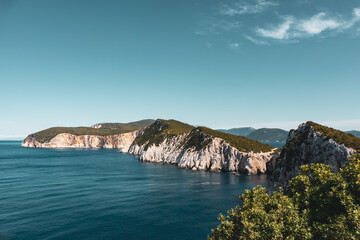 Fototapeta premium Panoramic view on vivid blue sea and steep green cliffs, sunny sea shore on a bright clear day in Greece. Scenic travel. Lefkada island, Ionian sea coast. Color graded