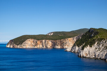 Vivid blue sea and steep rocky cliffs, sunny sea shore on a bright clear day in Greece. Scenic travel destination. Lefkada island, Ionian sea coast
