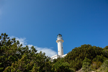 White lighthouse tall tower in greenery on a bright clear blue sky in Greece, Ionian sea. Scenic travel destination. Lefkada island