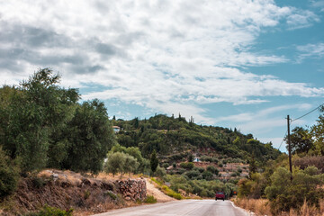 Scenic road to traditional Greek village with scenic cloudscape on green hills on Lefkada island, Greece. Travel Europe in summer by car