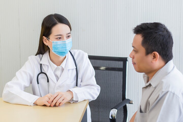 Young Asian woman doctor asking patient questions in the clinical examination room at the hospital by wearing a surgical mask at all times in health care and coronavirus protection concept.