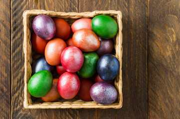 a large wicker box with festive Easter eggs on a wooden village table. top view.