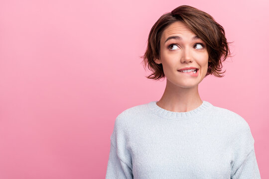 Photo of dreamy minded doubtful young woman look empty space think bite lips isolated on pink color background