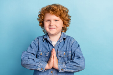 Photo of positive little ginger boy hold palms plead wear jeans jacket isolated blue color...