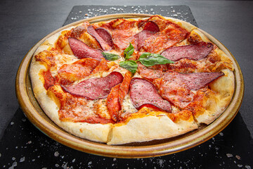 Italian salami pizza with cheese sauce and crispy pepper with roasted spice mix, wooden dish plate on a stone table top.