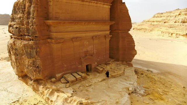 Aerial Reversing From A Woman Exiting An Ancient Tomb Carved Into The Side Of A Desert Rock Formation - Arabian Desert, Saudi Arabia