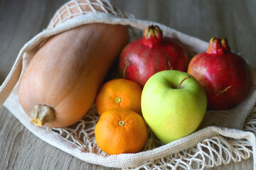 Crochet bag filled with butternut squash, pomegranates, apples and tangeriens. Selective focus.