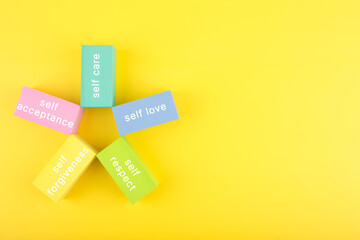 Mental health formula concept. Self acceptance, self care, self respect and self forgiveness written on flower from multicolored rectangles on yellow background with copy space