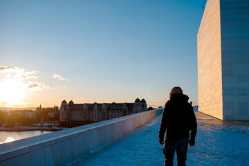 Rear view of traveler man in winter jacket walking teh sea coast on sunset - obrazy, fototapety, plakaty