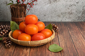 Ripe persimmons in a bamboo basket. Wooden table background with a set of persimmons on the left.