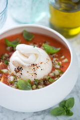 Close-up of gazpacho soup made of red tomatoes and served with burrata cheese in a white bowl, vertical shot, selective focus