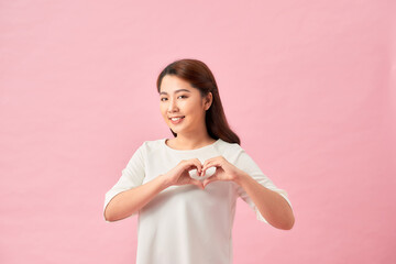 Closeup portrait smiling cheerful happy young woman making heart sign with hands isolated pink background