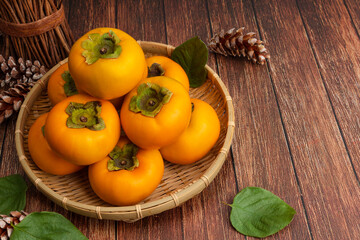 Sweet persimmons in bamboo basket. Top view, wooden table background and persimmon set.