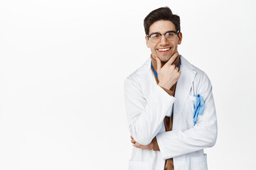 Smiling physician in medical robe, looking thoughtful and pleased, thinking of smth, standing over white background