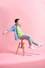 Fashionable young man sitting on stool against pink background