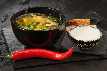 Chicken soup with vegetables in black bowl with red pepper on black background. Zeama - moldovan soup. Closeup.