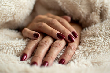 Wrinkled hand skin closeup. Dark red royal nail gel polish, female manicure, beauty treatment in a salon. Selective focus on the details, blurred background.