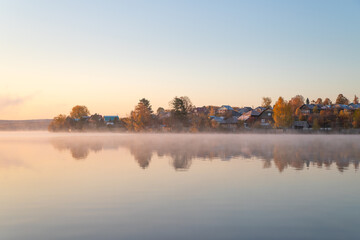Fototapeta premium Village in autumn on the shore of a pond in the morning
