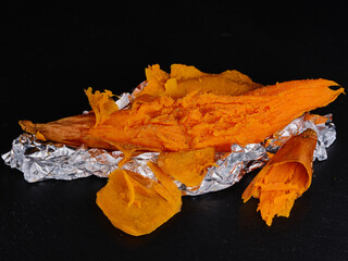 Sweet potato baked on dark stone. Rumpled aluminum foil