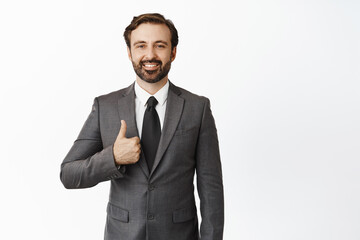 Business people. Handsome realtor, businessman showing thumb up and smiling, wearing suit, standing over white background