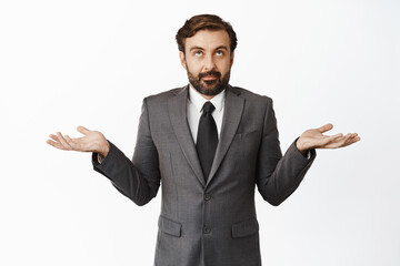 Clueless salesman in suit shrugging, spread empty hands sideways and looking up puzzled, confused what to do, dont know, standing over white background