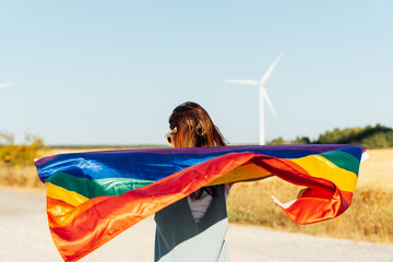 middle-aged beautiful young woman from behind in heolico park with windmills in the background from behind with lgtb flag. Liberty. equal rights