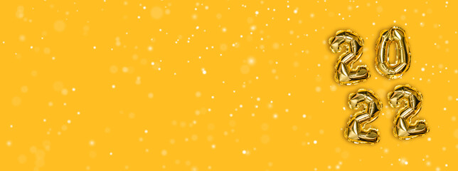 2022 golden foil balloons decor and Christmas snow on yellow background. New year concept with copy space.