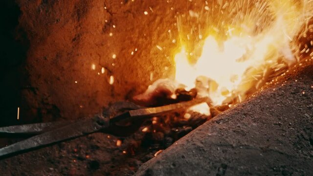Metal pliers turning metal piece in a hot furnace oven fire, sparks flying