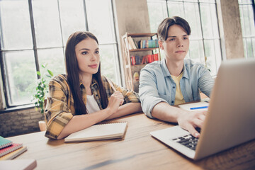 Photo of young two serious focused people college pupils students search information online in laptop prepare for exams indoors