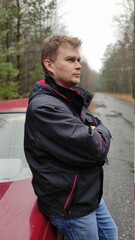 Young man near car on forest road in autumn
